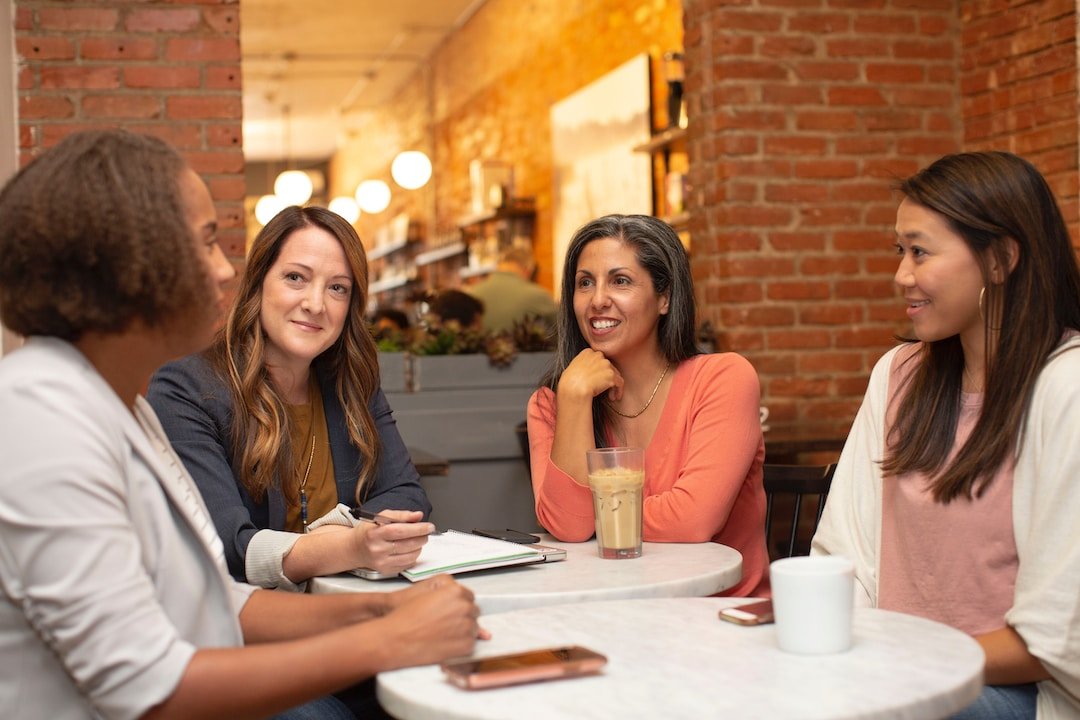 Four businesswomen sitting at two tables pushed together discussing sales leadership